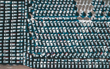 Naklejka premium Aerial top down view of new cars parked in car parking lot. Car dealer parking lot full of new automobiles. New cars lined up for import and export business.