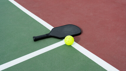 Pickleball paddle and ball laying on pickleball court.