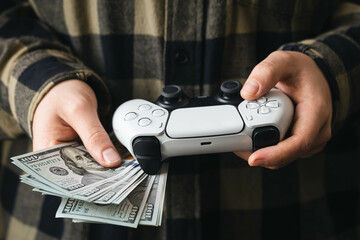A man plays a video game, a white gamepad and dollar bills in the hands of a man close-up. © sav_an_dreas