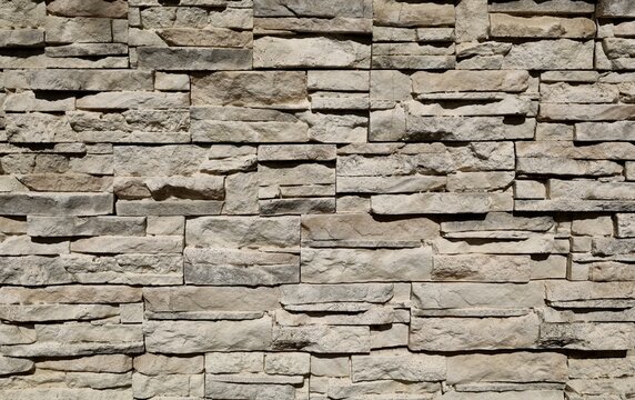 Old stone cladding wall made of striped stacked slabs of  gray brownish rocks. Outdoor coating. Background and texture.