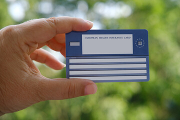 German health insurance card in female hand on natural green background, blue EU document...