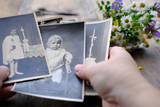 female hands hold old retro family photos over an album with vintage monochrome photographs in sepia color, genealogy concept, ancestral memory, family ties, childhood memories