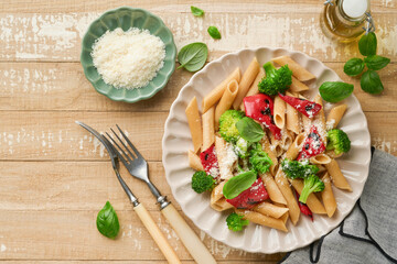 Wholegrain pasta penne with broccoli and red grilled bell pepper and on light wooden rustic background table. Vegan pasta. Traditional Italian cuisine. Flat lay. Copy space.