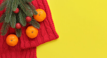 Red knitted scarf, tangerines and spruce branch on a yellow background, top view, copy space. Christmas composition, New Year, banner. New Year's branch with Christmas balls