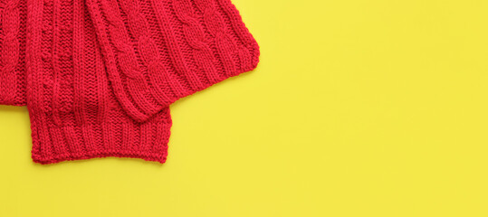Red knitted scarf on a yellow background, top view, copy space. Christmas scarf, clothing, accessory