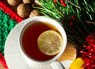 A cup of morning tea with lemon on a background of nuts, tangerines and green branches of a Christmas tree. Decorations for the New Year and Christmas.