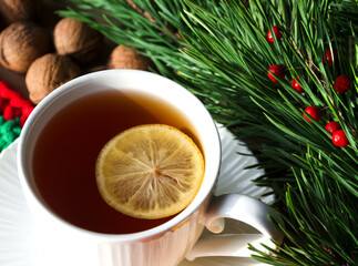A cup of morning tea with lemon and walnuts against a background of green branches of a Christmas tree. Decorations for the New Year and Christmas.