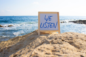 We listen symbol. Concept words We listen on white chalk background. Beautiful sea background. Business and We listen concept. Copy space.