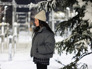 Young woman walking on walkway among snowy winter park at night.