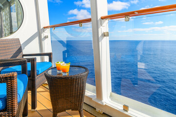 Two tropical mixed alcohol drinks sit on a small end table on the balcony veranda of a cruise ship...