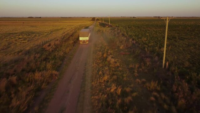 Un cami&oacute;n de carga transitando en un largo y polvoriento camino rural se va alejando grabado con un dron