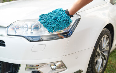 Hand in blue microfiber glove cleaning a white car s headlight.
