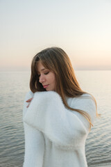 A serene evening beach portrait featuring a young and beautiful woman in a white cozy sweater. 
