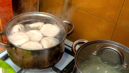 Khinkali are cooked in a saucepan with water in close-up against the background of a kitchen gas stove and a wall