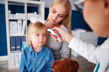 Doctor taking girl's temperature in medical practice