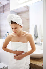 Young woman in bathroom suffering from stomach pain