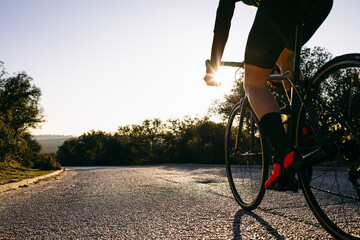 Close-up of athlete riding bicycle on country road at sunset