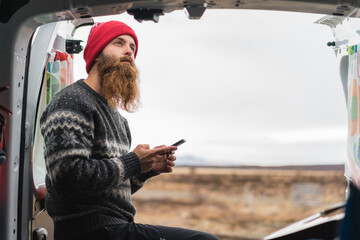 Portrait of pensive hipster standing at van with cell phone - obrazy, fototapety, plakaty