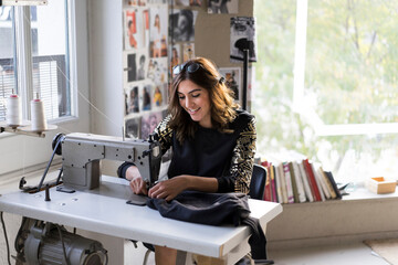 Smiling young fashion designer using sewing machine in her atelier