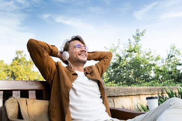 Laughing man sitting on bench listening music with headphones