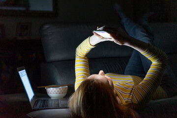 Young woman lying on the couch at home using smartphone
