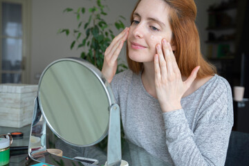 Young woman applying facial cream at home