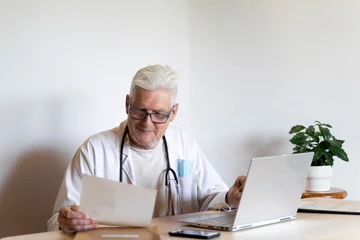 Poster Smiling doctor looking at medical record while sitting against wall © tunedin