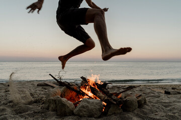 Man jumping over campfire at beach during sunset