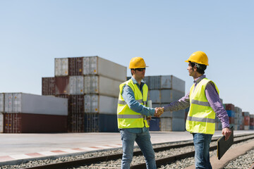 Workers shaking hands on railway tracks near cargo containers on industrial site