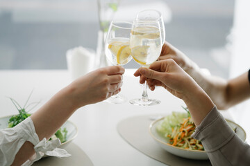 Close-up of three women toasting glasses of water in a restaurant - obrazy, fototapety, plakaty