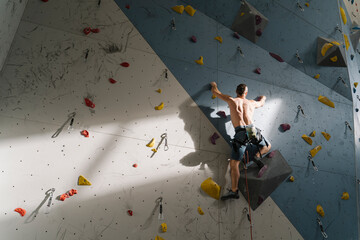 Shirtless man climbing on the wall in climbing gym