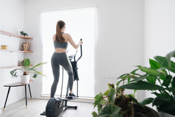 Woman performing workout on elliptical trainer at home - obrazy, fototapety, plakaty