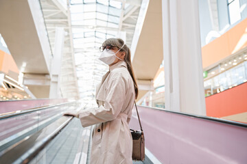 Woman with face mask and disposable gloves on an escalator in a shopping center