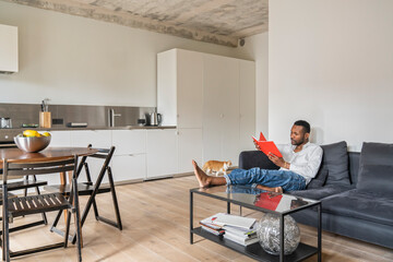 Man sitting on couch in modern apartment reading a book
