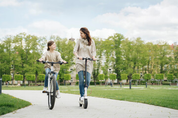 Girl cycling while mother riding electric scooter in city park © tunedin
