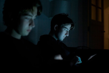 Two teenage boys using technology at home in the dark