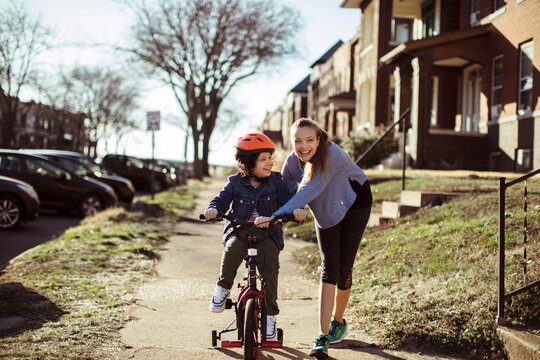 Caring young mother helping son ride a bicycle outdoors