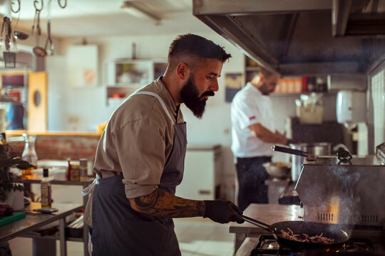 Focused Bearded Chef Cooking on a Stove in a Professional Kitchen