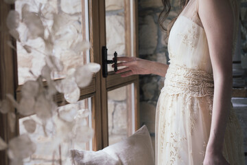 Young woman in elegant wedding dress opening window