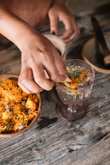 Hand of woman preparing fresh herbal tea with flower in glass on wooden table