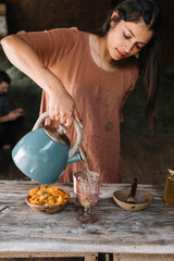 Beautiful woman pouring hot water in glass while preparing herbal tea on wooden table