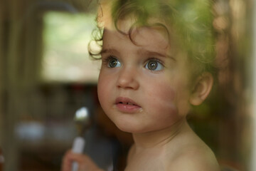Portrait of little girl behind windowpane eating