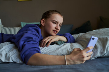 Portrait of girl lying on bed at home using smartphone for video chat