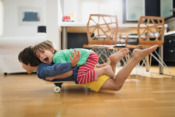 Two brothers at home lying on skateboard together having fun