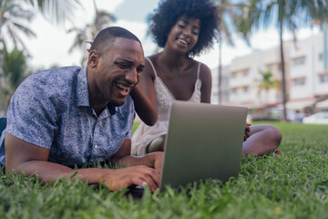 USA, Florida, Miami Beach, laughing young couple looking at laptop on lawn in a park - obrazy, fototapety, plakaty