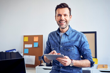 Portrait of smiling man using tablet in office - Powered by Adobe