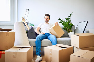 Frustrated man sitting on couch surrounded by cardboard boxes