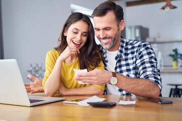 Couple sitting at dining table, using laptop, checking bills