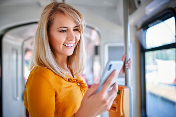 Smiling young woman using smartphone in a tram - obrazy, fototapety, plakaty