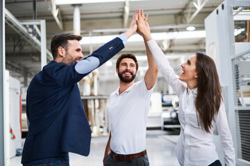Happy businessman and employees high fiving in a factory - obrazy, fototapety, plakaty